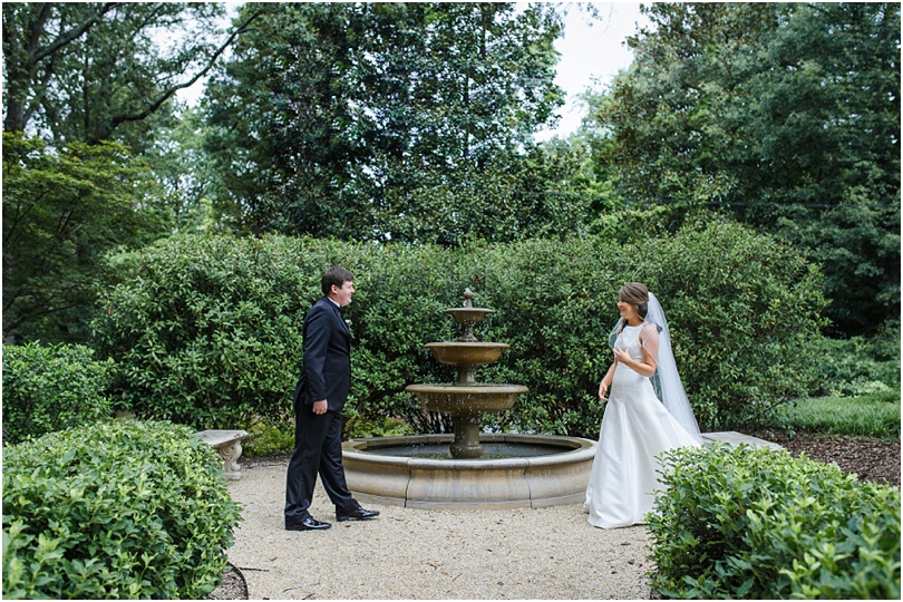 bride and groom having their first look by fountain of the estate wedding venue